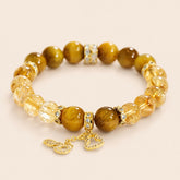 Tiger Eye and Golden Rutilated Quartz bracelet with gold-tone pavé spacers and dangling charms on a cream background