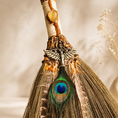 Close-up of handmade Peacock Feather Witch Broom with natural crystal, peacock feather, charm detail, and handwoven straw.