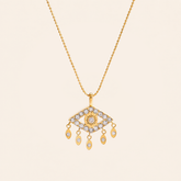 A gold-tone necklace featuring an evil eye pendant adorned with zircon, suspended from a delicate gold chain against a solid light beige background.