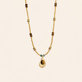 Tiger’s Eye pendant necklace with 18K gold-plated beaded chain and teal stone accents on a cream background