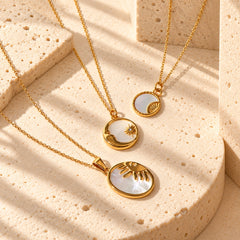 Gold-tone celestial shell pendant necklaces styled in a warm ivory studio, featuring natural shell inlay and sun and moon motifs