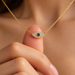 Close-up of petite gold-plated evil eye zircon pendant against a fingertip showing its small size and sparkling blue-centered design
