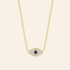 Gold-plated 925 sterling silver evil eye necklace with a blue center stone and zircon-set eye pendant against a light ivory background