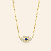 Gold-plated 925 sterling silver evil eye necklace with a blue center stone and zircon-set eye pendant against a light ivory background