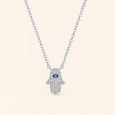 Front view of sterling silver Hamsa hand necklace featuring a blue evil eye motif and shimmering zircon stones on ivory background