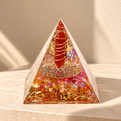 Red agate and citrine orgonite pyramid with copper coil and gold-tone details on a warm ivory stone surface