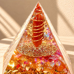 Red agate and citrine orgonite pyramid with red quartz and gold-tone details styled in warm natural sunlight