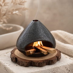 Black ceramic Palo Santo and sage burner with textured finish, open hearth design, flame, and smoke for energy cleansing rituals.