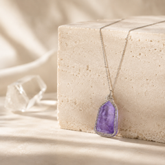 Amethyst pendant necklace on a beige stone block with a neutral background