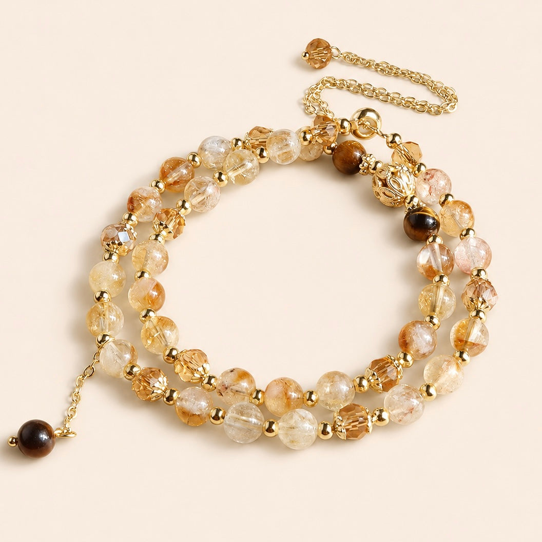 Citrine and Tiger’s Eye multi-strand bracelet with gold-tone chain and dangling stone charms on a cream background
