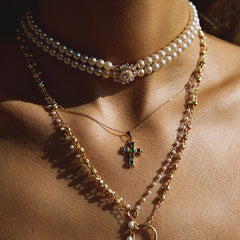 Close-up of a person wearing multiple necklaces with pearls and a cross pendant.