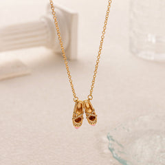 dainty pink ballet shoes necklace with gold chain on a soft white background