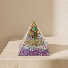 orgonite pyramid with green aventurine point, rose quartz chips, copper coil and gold totem on a neutral background