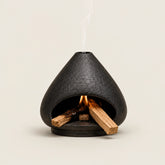 Black ceramic Palo Santo and sage burner with open hearth shape, burning wood, and smoke vent for indoor smudging rituals.