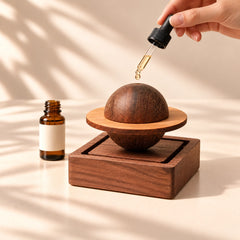 Glass dropper applying essential oil onto the Saturn-shaped wooden aroma diffuser