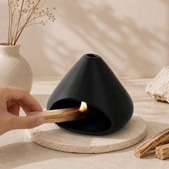 Hand lighting Palo Santo inside a matte black ceramic burner in a warm Wabi-Sabi setting