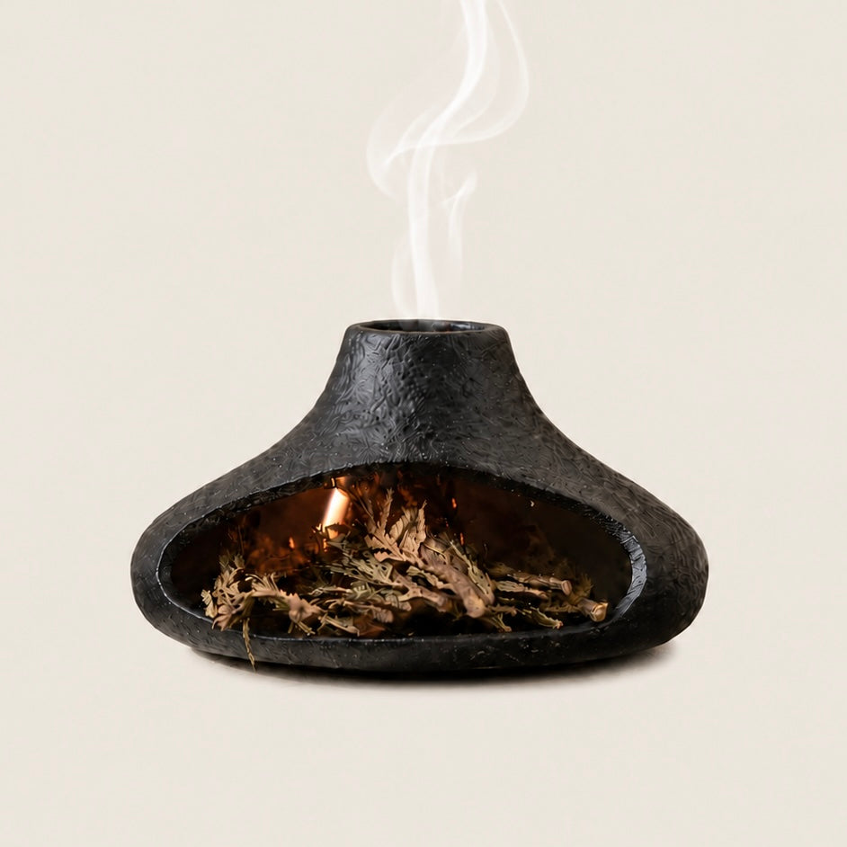Black chimney-style ceramic Palo Santo burner with dried sage and smoke on a warm ivory background