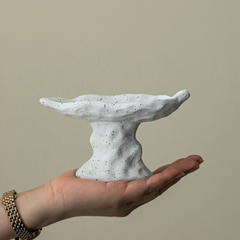 Hand holding a small, textured stone-like sculpture against a plain background