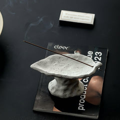 Ceramic incense holder with a lit incense stick on a magazine