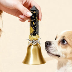 Hand holding a black celestial crystal point ritual bell with engraved sun and moon patterns, gold bell base, shown next to a small dog in a calm indoor setting.