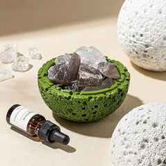 Green volcanic-texture bowl holding clear and smoky crystals beside essential oil