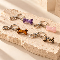 Four natural stone pet bone charms in Amethyst, Rose Quartz, Tiger's Eye and Dalmatian Jasper arranged on a warm ivory stone slab