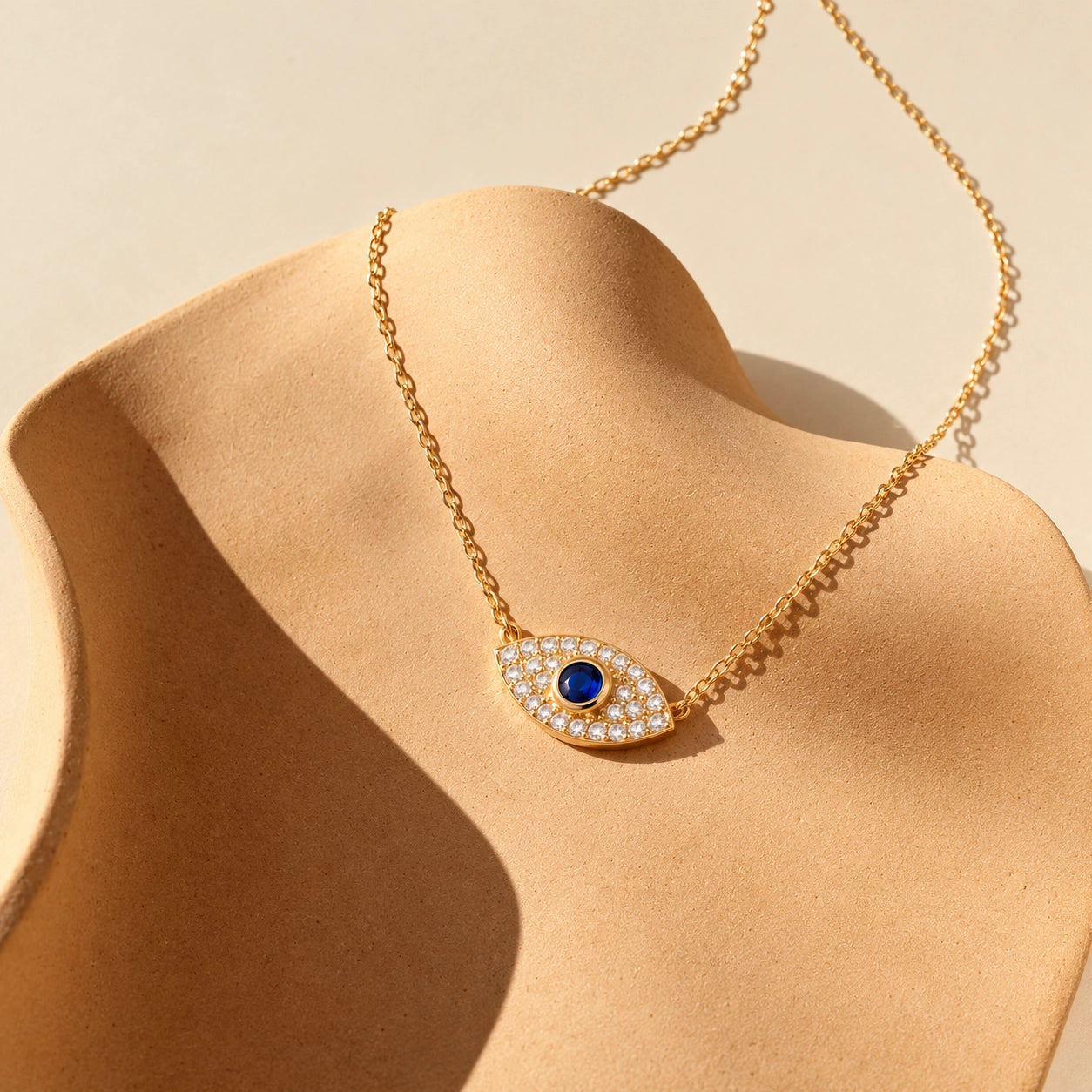 Gold-plated sterling silver evil eye necklace with a deep-blue center stone and zircon detailing on an ivory sculptural display