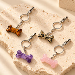 Four natural stone pet bone charms in Amethyst, Rose Quartz, Tiger's Eye and Dalmatian Jasper displayed on a warm ivory stone slab, alternate angle