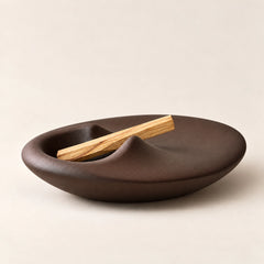 Low side view of a sculptural brown concrete Palo Santo holder with an organic curved silhouette