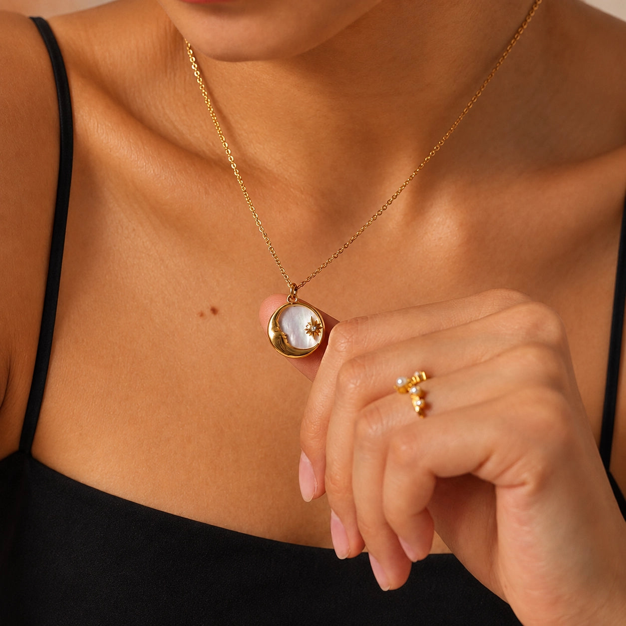 Model gently holding a gold-tone celestial shell pendant necklace to show its delicate size and natural shell detail