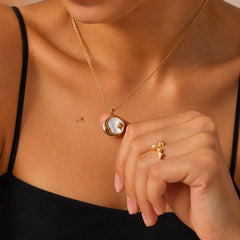 Model gently holding a gold-tone celestial shell pendant necklace to show its delicate size and natural shell detail