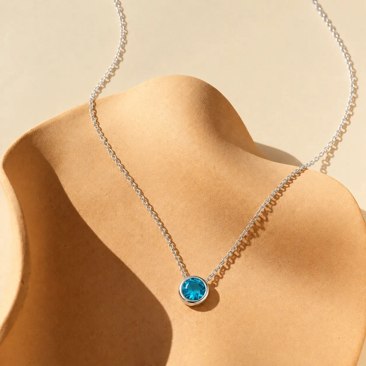 925 sterling silver blue zircon necklace with brilliant teal-blue round pendant displayed on a curved warm sand-colored sculptural surface