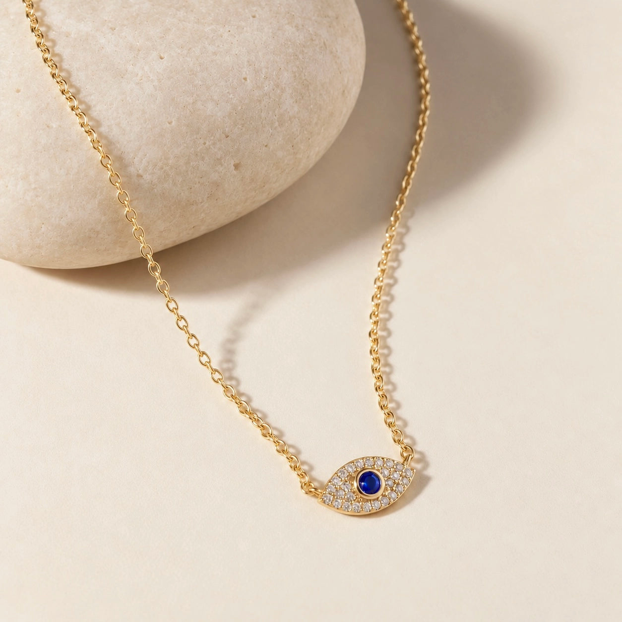 Gold-plated evil eye necklace in 925 sterling silver with sparkling zircon details and blue center stone styled on a smooth ivory stone