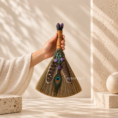 Handmade amethyst peacock feather witch broom held in hand to show its approx. 35 cm size, with natural straw, crystal points and wrapped handle