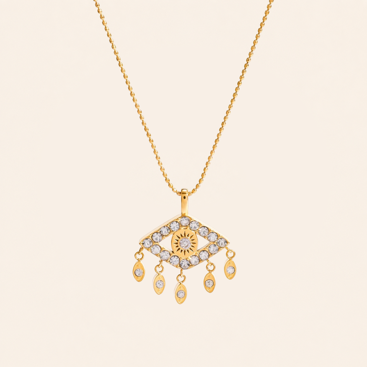 A gold-tone necklace featuring an evil eye pendant adorned with  zircon, suspended from a delicate gold chain against a solid light beige background.