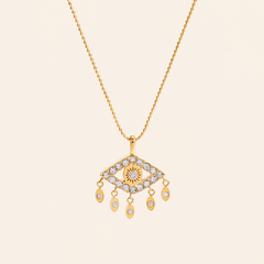 A gold-tone necklace featuring an evil eye pendant adorned with  zircon, suspended from a delicate gold chain against a solid light beige background.