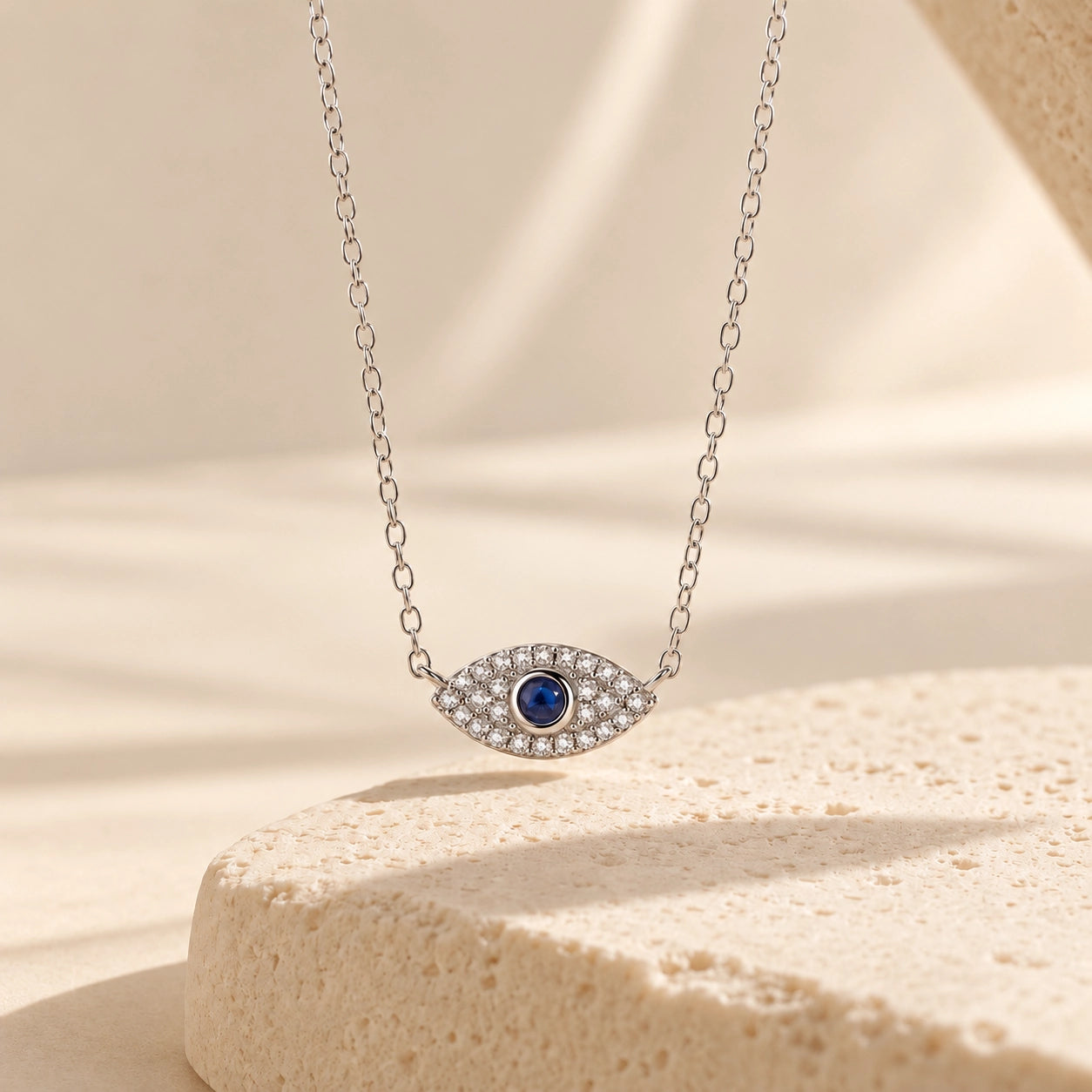 Silver sterling silver evil eye necklace with blue center stone and zircon accents displayed above a textured ivory pedestal