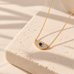 Gold-plated sterling silver evil eye necklace with zircon-set pendant on a textured cream stone plinth in natural light