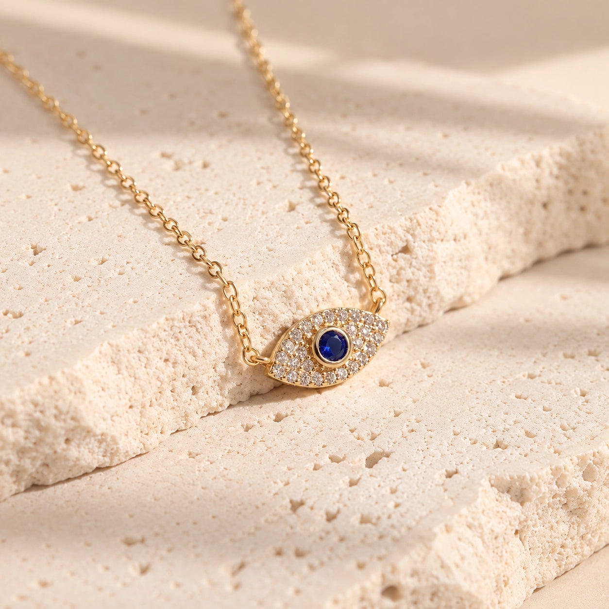 Detailed view of gold-plated evil eye necklace with zircon accents and blue center stone between warm ivory stone surfaces