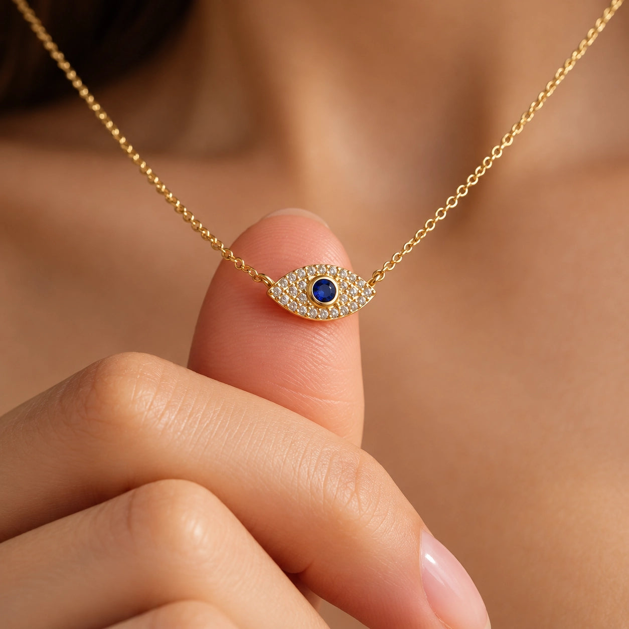 Close-up of petite gold-plated evil eye zircon pendant against a fingertip showing its small size and sparkling blue-centered design