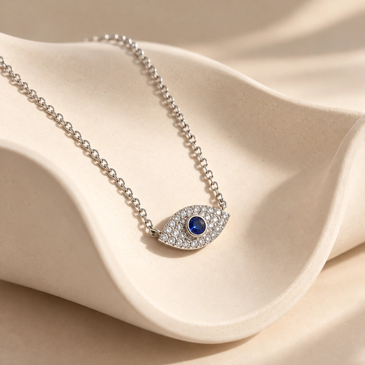 Silver 925 sterling silver evil eye necklace with blue center stone and zircon accents on a sculptural ivory ceramic surface
