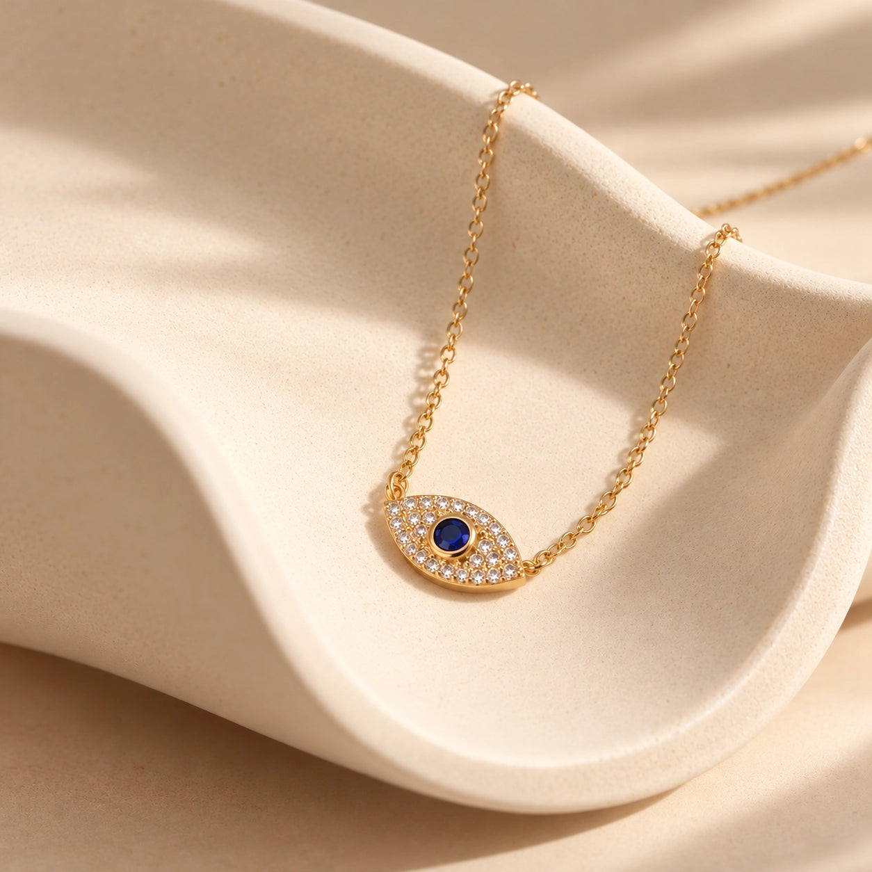 Gold-plated 925 sterling silver evil eye necklace with deep-blue center and zircon-set details displayed on a curved ivory ceramic sculpture