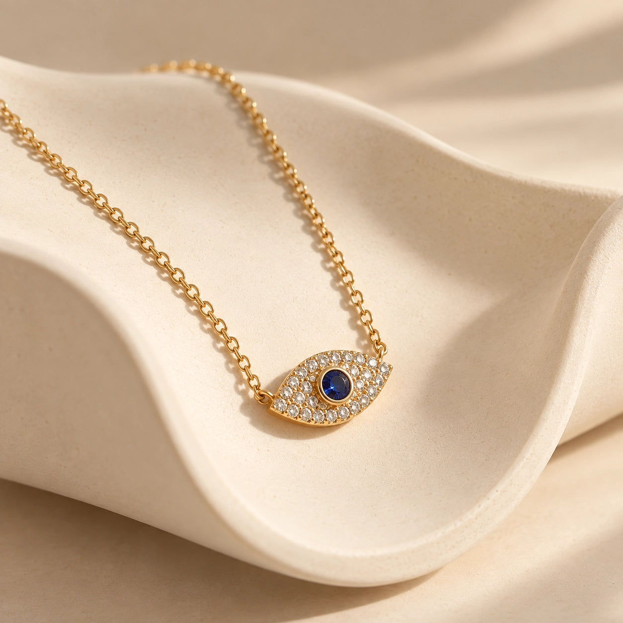 Close-up of gold-plated evil eye pendant with blue center stone and sparkling zircon settings on an ivory ceramic display