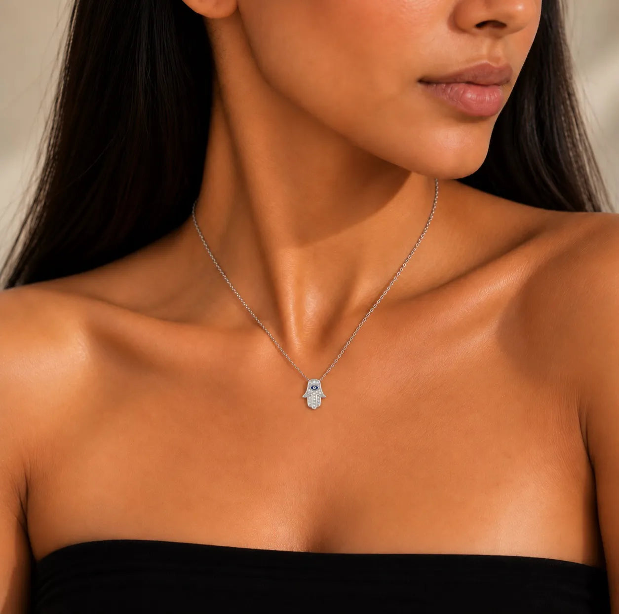 Close-up model styling of a dainty silver Hamsa hand necklace with blue evil eye detail and shimmering zircon
