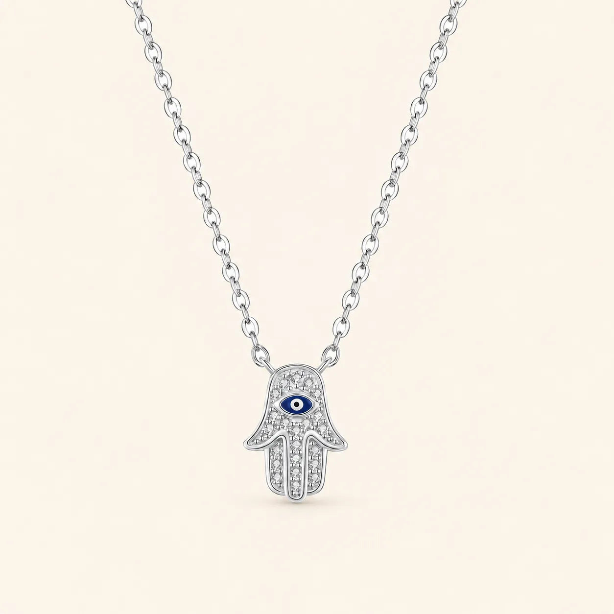 Front view of sterling silver Hamsa hand necklace featuring a blue evil eye motif and shimmering zircon stones on ivory background