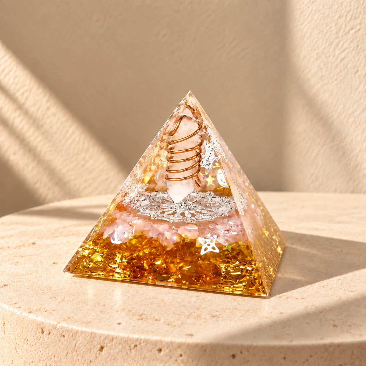 Rose quartz, clear quartz and citrine orgonite pyramid on a warm ivory stone surface in natural sunlight