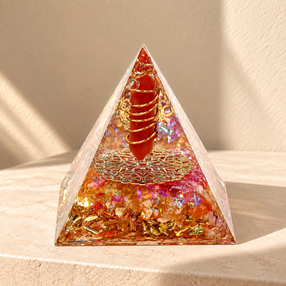 Red agate and citrine orgonite pyramid with copper coil and gold-tone details on a warm ivory stone surface
