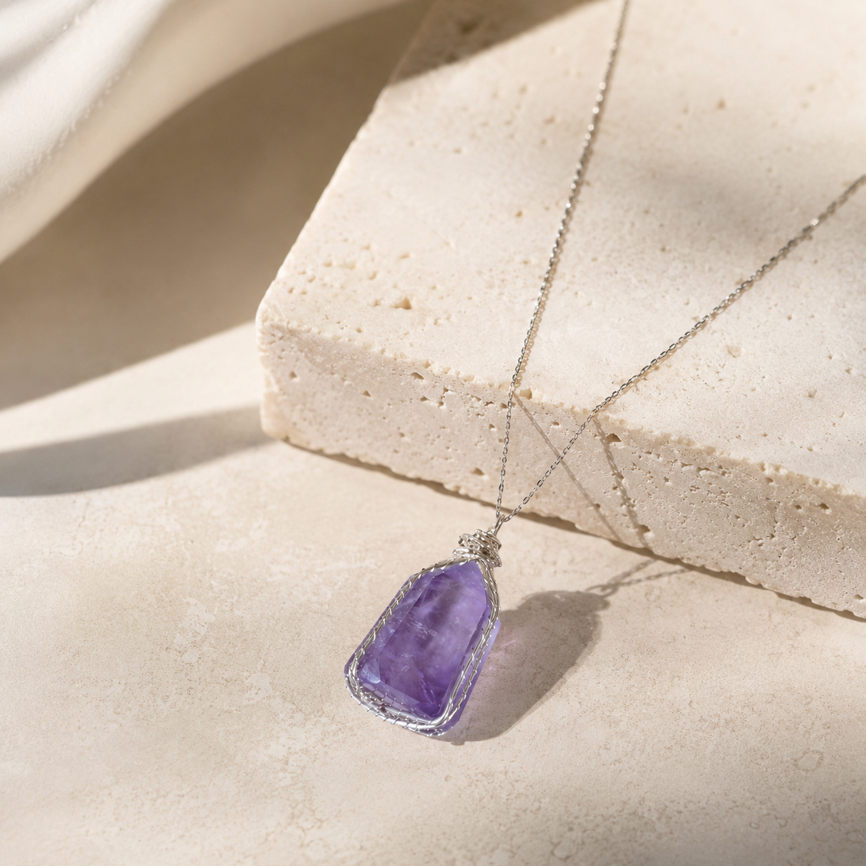 Amethyst pendant necklace on a beige stone surface