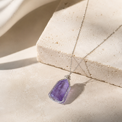 Amethyst pendant necklace on a beige stone surface