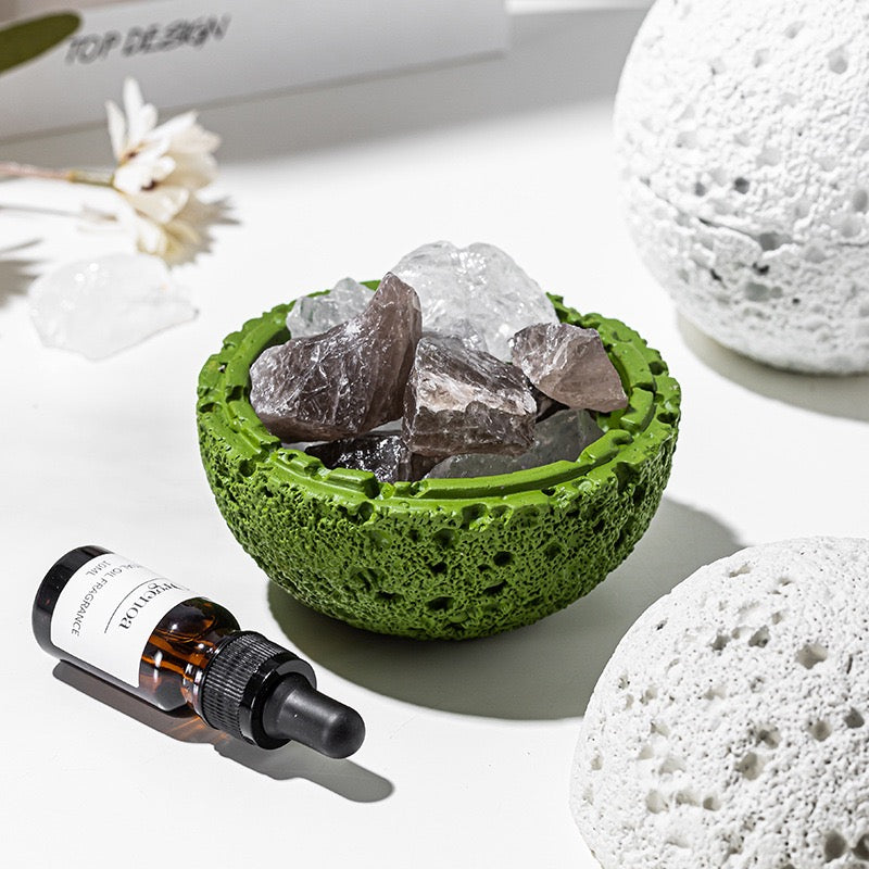Green textured bowl with crystals, a dropper bottle, and white stones on a light surface.
